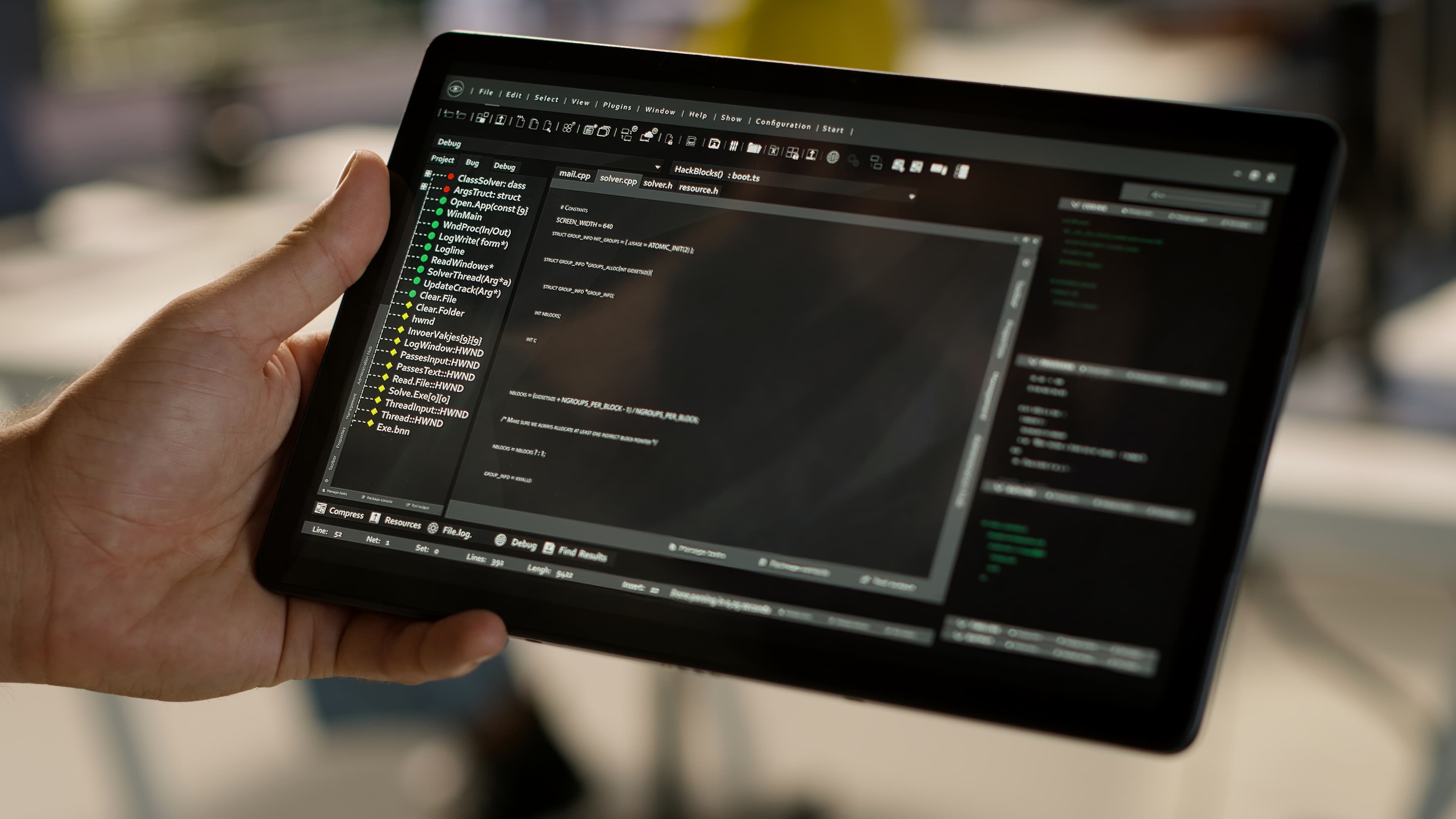 Mão segura um tablet com editor de código aberto, num ambiente claro e desfocado.